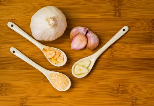 Garlic bulb with garlic flakes ,garlic salt, garlic cloves and sliced garlic on a wooden bamboo chopping board 