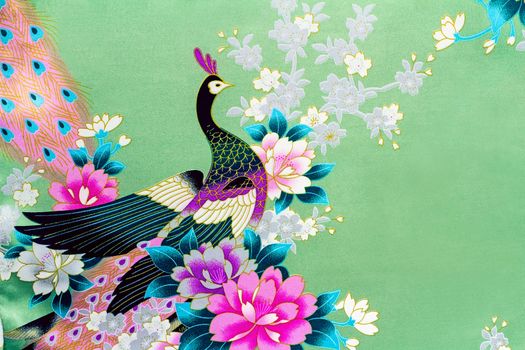 Beautiful silk fabric of light green color with the bright image of a peacock among flowers.g