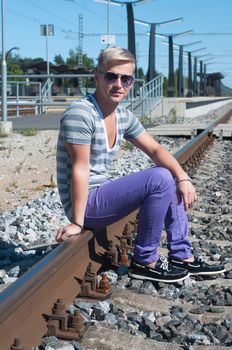 Attractive young guy in sunglasses sitting on the rails