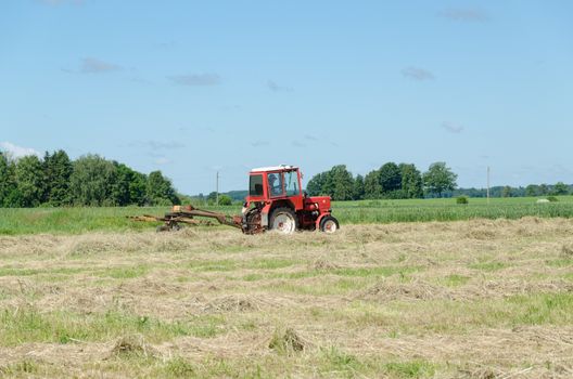 tractor heavy machine equipment ted hay dry grass in agriculture field. Preparing fodder feed for animals.