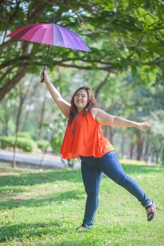 Happy fatty asian woman with umbrella outdoor in a park