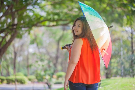 Happy fatty asian woman with umbrella outdoor in a park