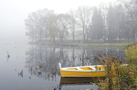 yellow wooden boat on autumn lake and early morning mist