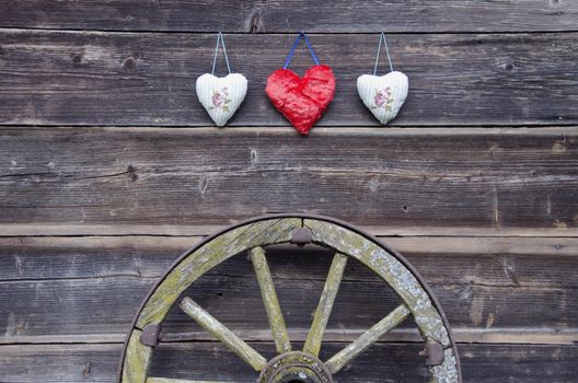 old barn wooden wall with three hearts and ancient carriage wheel