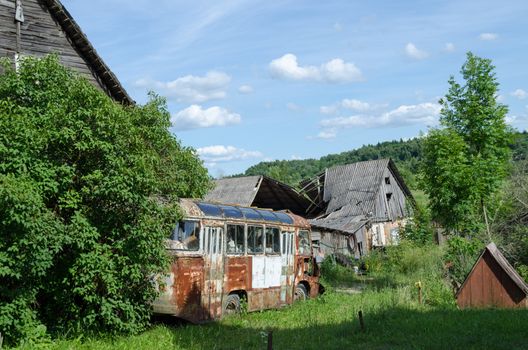 old rusty broken passenger bus stand along country rotten house in summer time