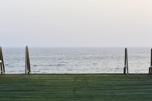 Wooden pier with metal handrails on the background of sea and sky