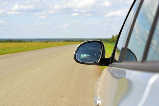 View on car mirror. Summer landscape with green grass, road and clouds