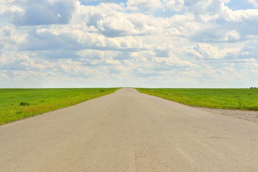 Summer landscape with green grass, road and clouds