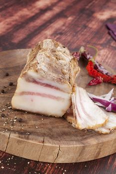 Big bacon piece and slices on wooden chopping board on wooden background. Traditional meat eating. 