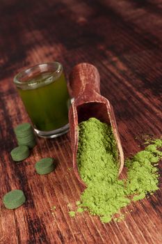 Nutritional supplements chlorella, spirulina and wheat grass on wooden background. Pills, green drink and ground powder. Green superfood. Alternative medicine and detox. 