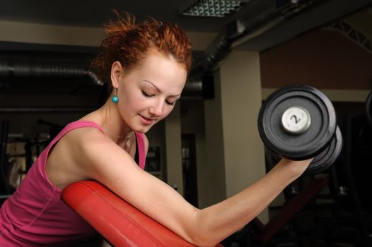 Girl doing biceps exercise with dumbbell in the gym