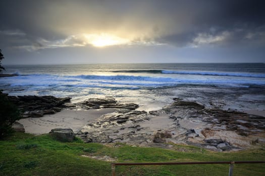 The sound of rain and ocean waves and the sun peeks through throwing some light on the scene.  Cronulla, Australia