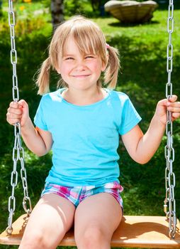 Little girl sitting on a swing at summer park