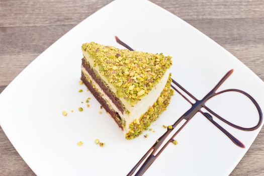 Pistachio cake on a white plate on wooden surface.