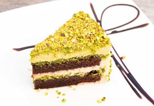 Pistachio cake on a white plate on wooden surface.