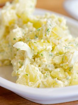 Delicious Freshly Made Creamy Potato Salad on White Plate closeup on Wooden background