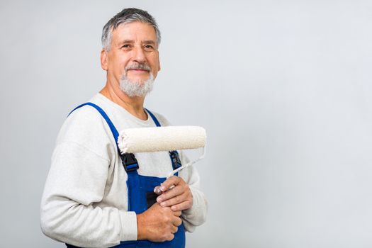 Senior man posing with a paint roller after having paint a white wall