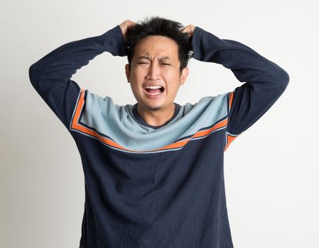 Portrait Of Mad Asian Man Pulling His Hair On Plain Background