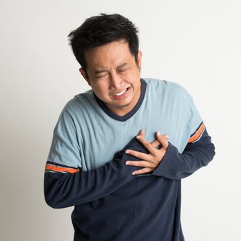 Asian male heartache, pressing on chest with painful expression, on plain background