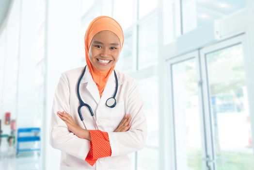 Cheerful young Muslim female doctor portrait, standing inside hospital