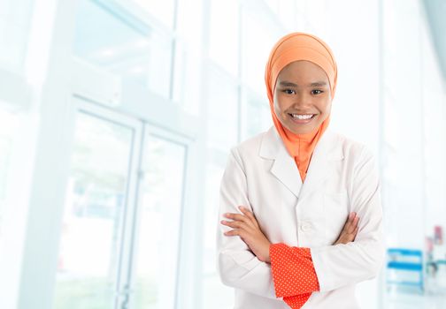 Cheerful young Muslim female nurse portrait, standing inside hospital
