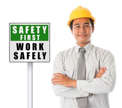 Asian male worker wearing a hardhat smiling and looking at camera, arms crossed standing beside safety first sign board, isolated on white background.