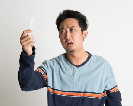 Southeast Asian man checking on a comb with shock facial expression, on plain background.