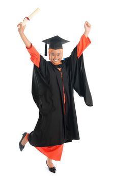 Portrait of full length smiling Asian female Muslim student in graduate gown hands raised showing graduation diploma jumping isolated on white background.