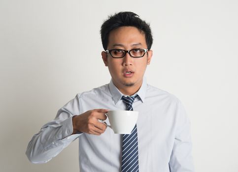 Tired Asian businessman with dark eyes circle holding coffee cup on plain background