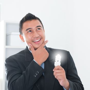 Southeast Asian businessman holding an illuminated light bulb, thinking in office.