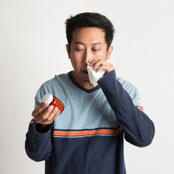 Asian male sneezing and holding medicine bottle, on plain background