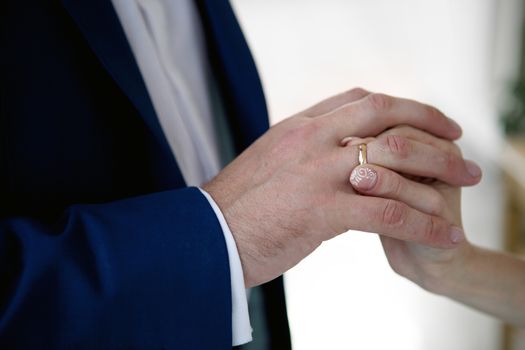 hands of a bride and a groom, woman putting a wedding ring on the finger of her groom