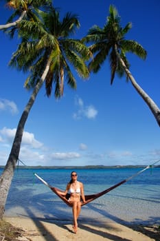 Young woman in bikini sitting in a hammock between palm trees, Ofu island, Vavau group, Tonga