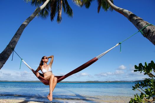 Young woman in bikini sitting in a hammock between palm trees, Ofu island, Vavau group, Tonga