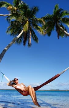 Young woman in bikini sitting in a hammock between palm trees, Ofu island, Vavau group, Tonga