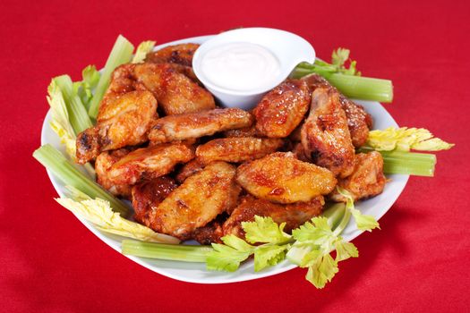 Buffalo chicken wings on plate with blue cheese sauce and celery.