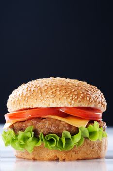 Cheeseburger with tomatoes and lettuce on black background