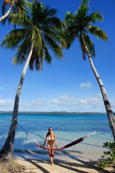 Young woman in bikini standing by the hammock between palm trees, Ofu island, Vavau group, Tonga