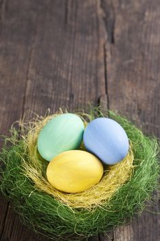 Colorful easter eggs in nest on wooden background 