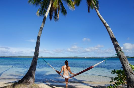 Young woman in bikini sitting in a hammock between palm trees, Ofu island, Vavau group, Tonga