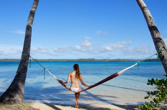 Young woman in bikini sitting in a hammock between palm trees, Ofu island, Vavau group, Tonga