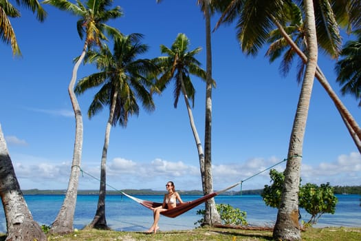 Young woman in bikini sitting in a hammock between palm trees, Ofu island, Vavau group, Tonga