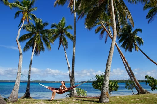 Young woman in bikini sitting in a hammock between palm trees, Ofu island, Vavau group, Tonga