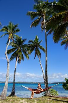 Young woman in bikini sitting in a hammock between palm trees, Ofu island, Vavau group, Tonga