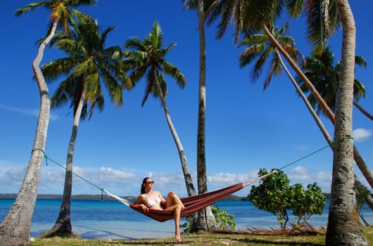 Young woman in bikini sitting in a hammock between palm trees, Ofu island, Vavau group, Tonga