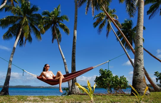 Young woman in bikini sitting in a hammock between palm trees, Ofu island, Vavau group, Tonga