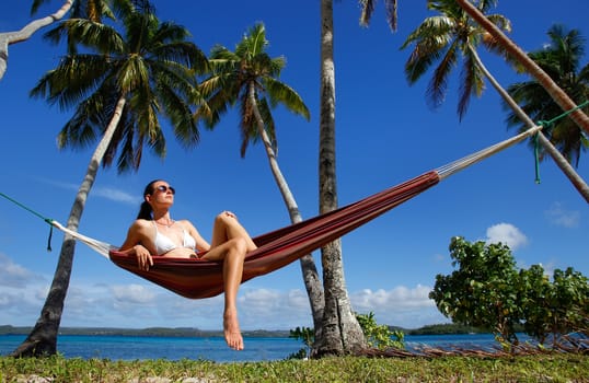 Young woman in bikini sitting in a hammock between palm trees, Ofu island, Vavau group, Tonga