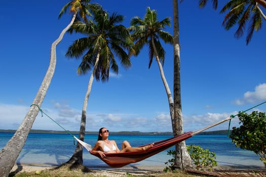 Young woman in bikini sitting in a hammock between palm trees, Ofu island, Vavau group, Tonga