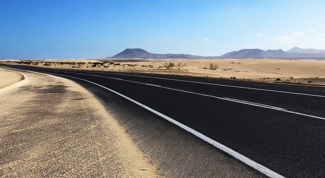 Winding road through the dunes of Corralejo desert with volcano in the background, in Fuerteventura, Canary Islands, Spain.