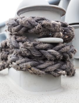 Close-up of a mooring rope with a knotted end tied around a cleat on a wooden pier/ Nautical mooring rope